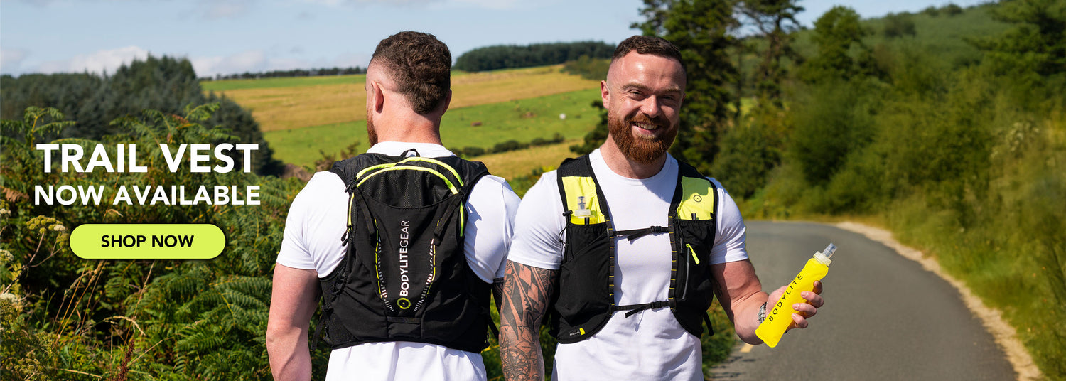 Two men wearing trail vests on a road with greenery in the background