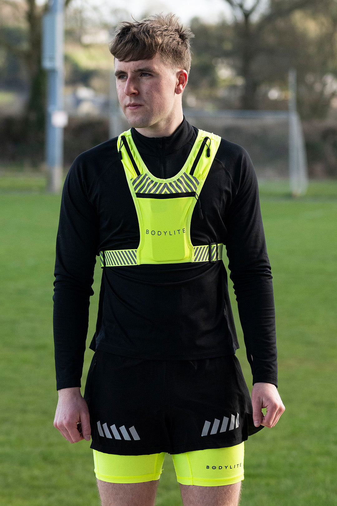 A person wearing a neon yellow and black phone holder vest and shorts with reflective details.