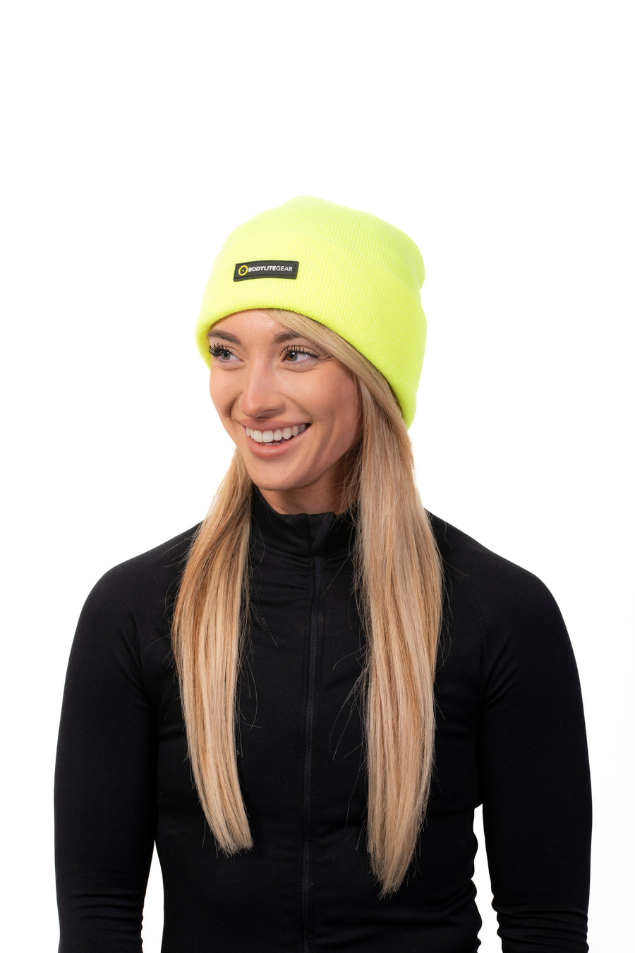 A woman wearing a neon yellow beanie and a black jacket. She is smiling and standing against a white background.