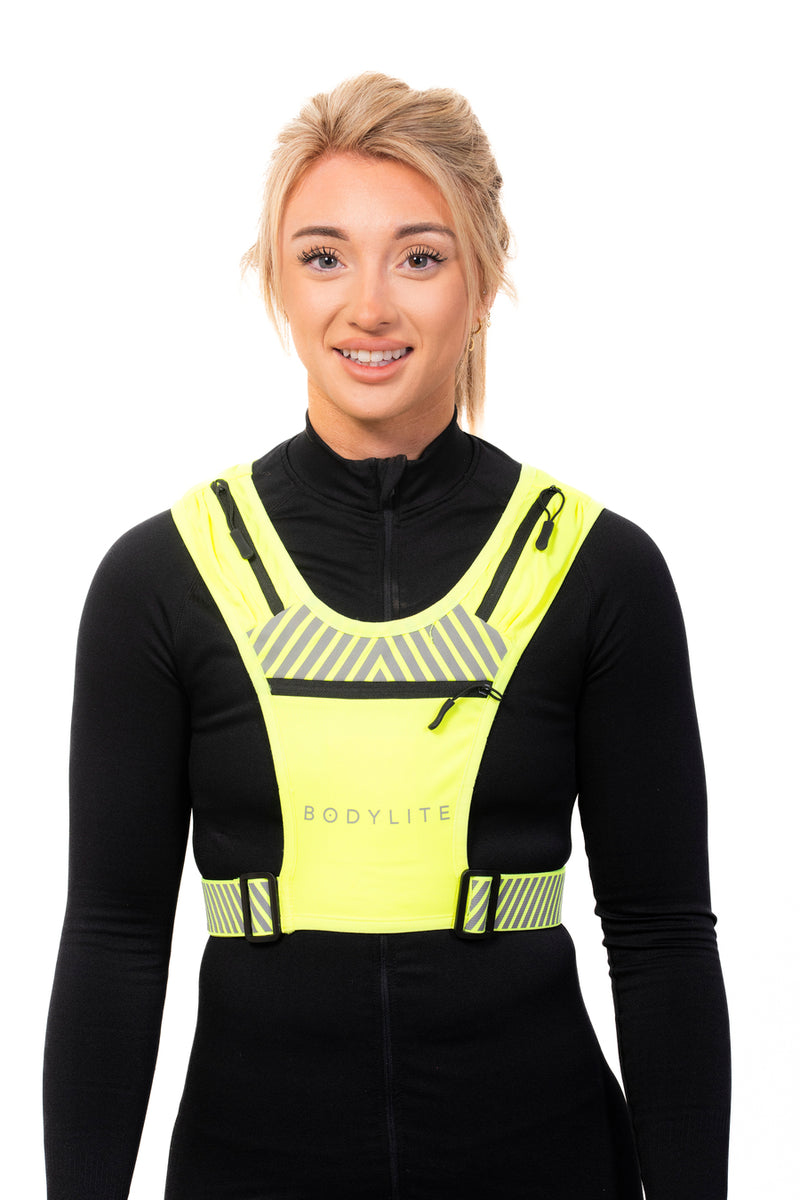 A person wearing a neon yellow phone holder vest with reflective straps and detailing, designed for visibility during workouts.
