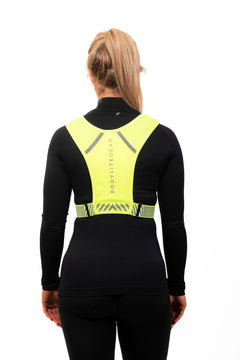 A person wearing a neon yellow phone holder vest with reflective straps and detailing, designed for visibility during workouts. this is the back view
